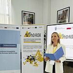Uczestniczka PHD RISK Summer School prezentuje materiały podczas wydarzenia w sali konferencyjnej, z bannerami i ekranami w tle.