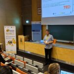 Prezentacja na konferencji PHD RISK Summerschool w sali wykładowej, z uczestnikami słuchającymi wykładu i korzystającymi z laptopów.